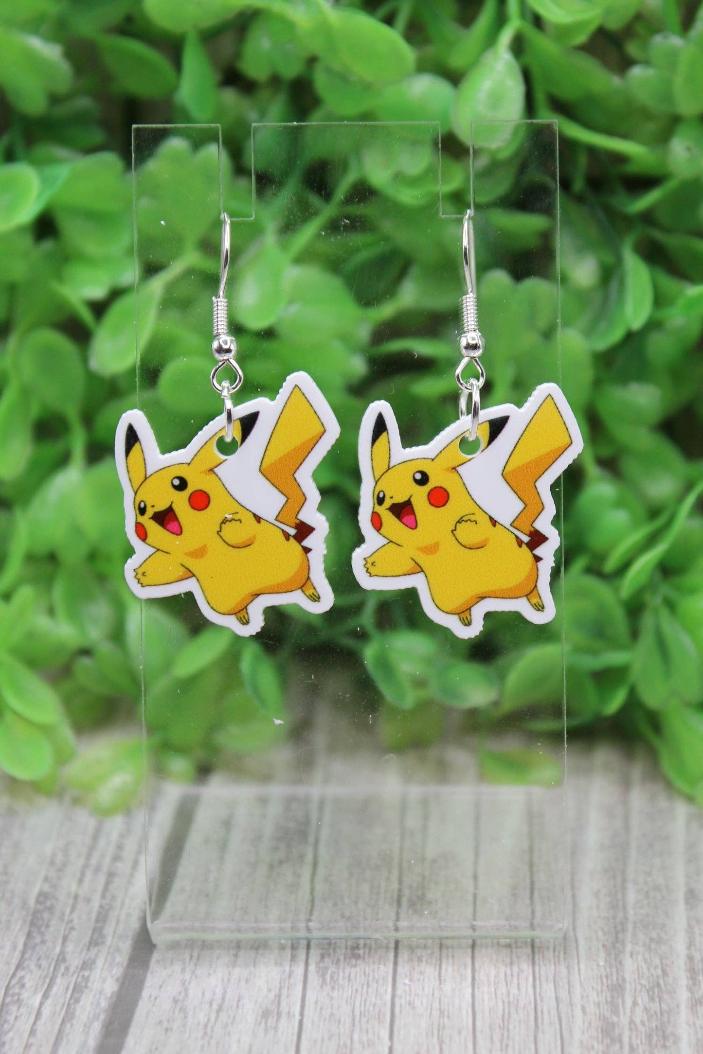 Pikachu earrings on a clear stand with a green leafy background