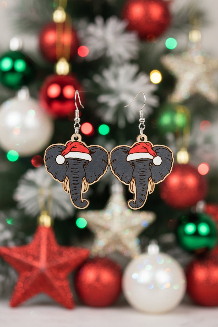 Earrings shaped like elephants wearing Santa hats on a wooden card with 'Hylidae Boutique' branding.